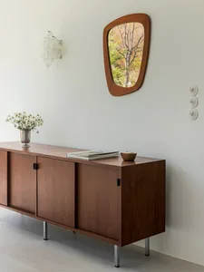 A mid-century modern sideboard made of wood with a vase of white flowers, books, and a small bowl on top.
