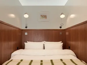 A minimalist bedroom with wooden paneled walls, white bedding, and two wall-mounted lamps.