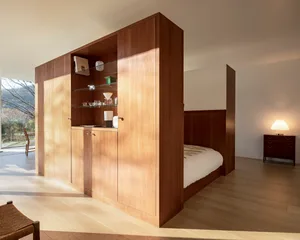 Modern minimalist bedroom with wooden cabinets, glass shelves, and a bed.