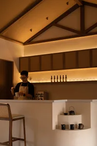 A minimalist coffee bar made of wood and concrete features a barista preparing coffee.