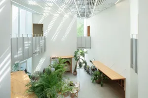 A minimalist restaurant lobby featuring wooden furniture and glass partitions, with a high ceiling and ample natural light.