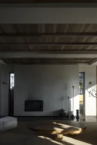 A modern living room with a wooden table, minimalist decor, and wooden ceiling beams.