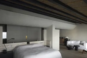 A modern minimalist bedroom with concrete walls and floor, featuring a large bed, a white sofa, and a wooden floor.