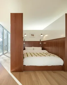 A minimalist bedroom with a wooden bed platform and paneling, featuring a cozy white bed and ambient lighting.