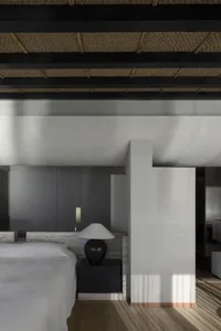 A modern minimalist bedroom featuring a large bed with a concrete frame and a black lamp on a nightstand.