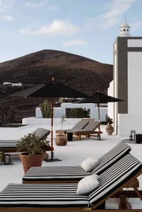 A modern residential patio with concrete and wooden furniture and black and white striped cushions.