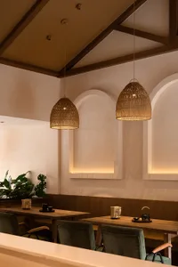 A photograph of a modern restaurant interior featuring wooden furniture and woven basket lamp shades.