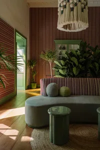 A modern living room featuring a striped sofa adorned with round cushions and surrounded by green plants and a textured cloth