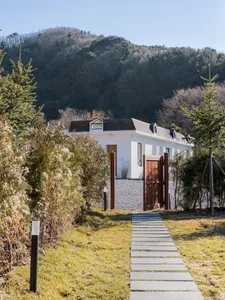 A modern home with white stucco walls and black metal accents, featuring a stone pathway and a wooden gate.
