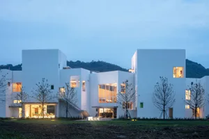 A modern house with white stucco exterior at dusk, featuring large windows and a garden.
