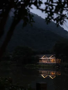 Rustic residential architecture with wooden materials reflecting on a serene lake at dusk.