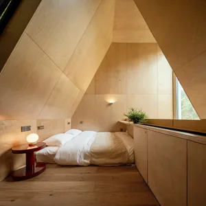 Modern minimalist bedroom with wooden walls, floor, and furniture, featuring a comfortable bed with white bedding and a singl