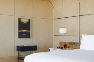 A minimalist bedroom with a white bed, wood wall panels, and a hanging lamp.