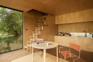 Minimalist kitchen with a natural wood finish, featuring a round table and chairs, a kitchen counter with cabinets, and a lad