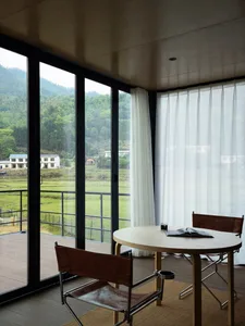 簡約客廳搭配木質家具、大型窗戶，以及綠意山丘與田野景觀。