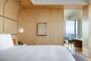 A modern bedroom with a bed, a chair, and a desk overlooking a cityscape.