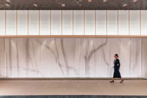 A woman walks past a modern lounge area featuring concrete tiles and glass elements.