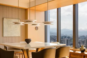 A modern minimalist dining room featuring a white table, leather chairs, pendant lights, and a view of mountains through larg