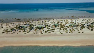 Aerial view of modern buildings on a sandy beach with clear blue waters.