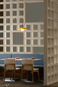 A modern restaurant booth with blue upholstery and metal accents, featuring a yellow pendant light and a glass wall