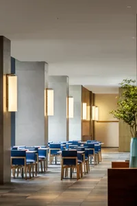 Modern restaurant interior featuring concrete pillars, wooden furniture, and blue chairs.