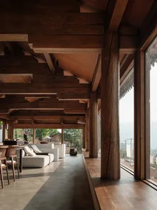 A spacious, industrial-style living room with exposed wooden beams and a large window overlooking a serene landscape.