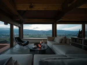 A minimalist living room with a large window showcasing a scenic mountain view, featuring wooden beams, white sofas, and a co