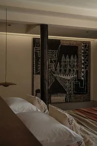 A bedroom featuring modern art decor with a wooden column, black and white abstract painting, and beige bedding.