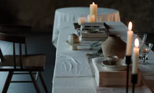 A modern dining table set with candles, books, and ceramic containers.