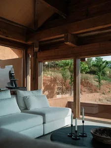 A modern living room with a white sofa, concrete floor, and large windows overlooking a natural landscape.