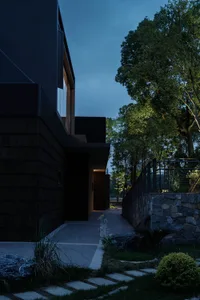 Modern residential exterior with concrete and glass materials, illuminated by soft ambient lighting.