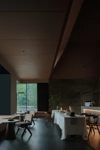 A modern restaurant dining room featuring stone flooring, sleek furniture, and natural light.