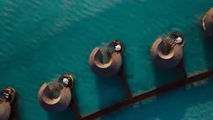 Aerial view of circular waterfront huts with thatched roofs and glass walls.