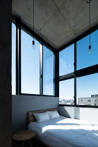 A minimalist bedroom with concrete walls, large windows, and white bedding.