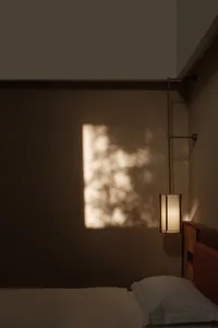 A minimalist bedroom with a grey wall, a bed with white bedding, and a hanging light fixture casting a warm glow on the wall.