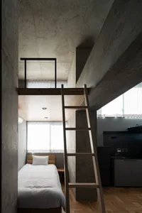 A modern concrete bedroom with a wooden ladder leading to a loft area.