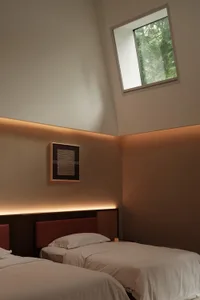 A minimalist bedroom with two beds, white bedding, and a skylight.