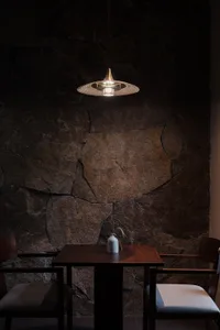 Modern restaurant interior featuring stone wall, wooden table, and pendant light.