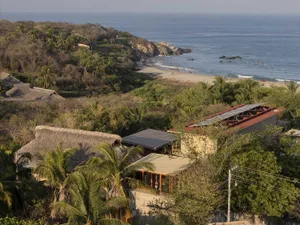 Aerial view of beachside residences featuring mixed materials such as thatched roofs and stone walls.