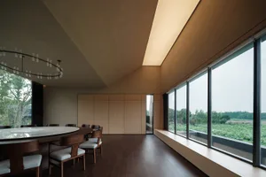 A minimalist dining room with wood accents, featuring a round table and chairs with white cushions.