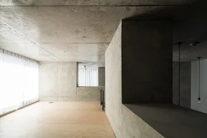 Minimalist living room with concrete walls and floor, featuring geometric shapes and natural light.