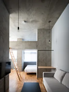 A minimalist living room featuring concrete walls, wooden flooring, and metal accents.