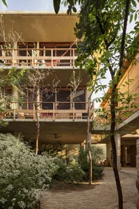 A modern residential house with a concrete and wooden exterior, featuring a courtyard with greenery.