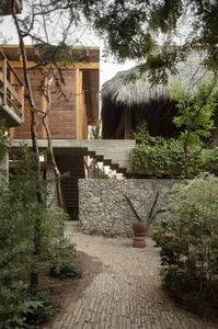 A modern residential building with wooden structures, stone walls, and thatched roofs surrounded by greenery.