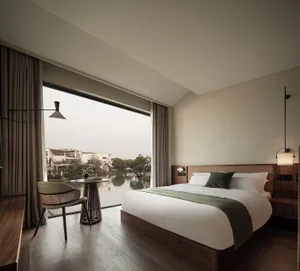 A modern bedroom featuring a cozy bed with white bedding, green throw pillows, and a wooden floor, looking out onto a scenic