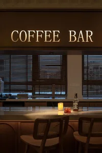 Modern coffee bar with illuminated counter and wooden chairs.