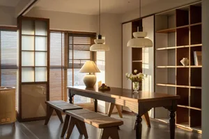 A cozy dining room featuring wooden and wicker furniture, a table with lamps, and a bookshelf with a vase.