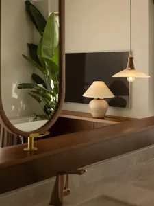 Modern bathroom interior featuring wooden vanity, ceramic lamp, glass pendant light, and green plant.