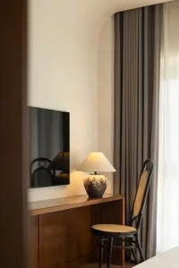 A modern workspace featuring a wooden lamp with a white shade, a black steel and canvas chair, and a flat-screen TV on a buil