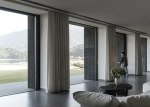 A modern living room featuring glass curtains and a scenic view of distant mountains and a body of water.